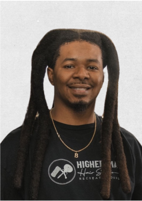 A man with dreadlocks and a goatee, smiling, wearing a black T-shirt and a gold necklace with a 'B' pendant, against a light-colored background.