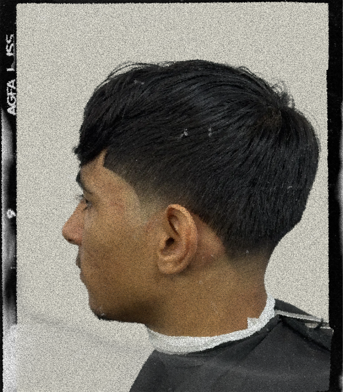 Side view of a person with short black textured hairstyle, faded on the sides and longer on top, wearing a black cape in a barbershop.