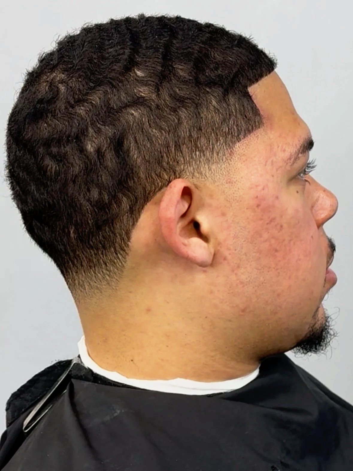 Side profile of a young man with a fresh fade haircut with patterned designs shaved into the sides.
