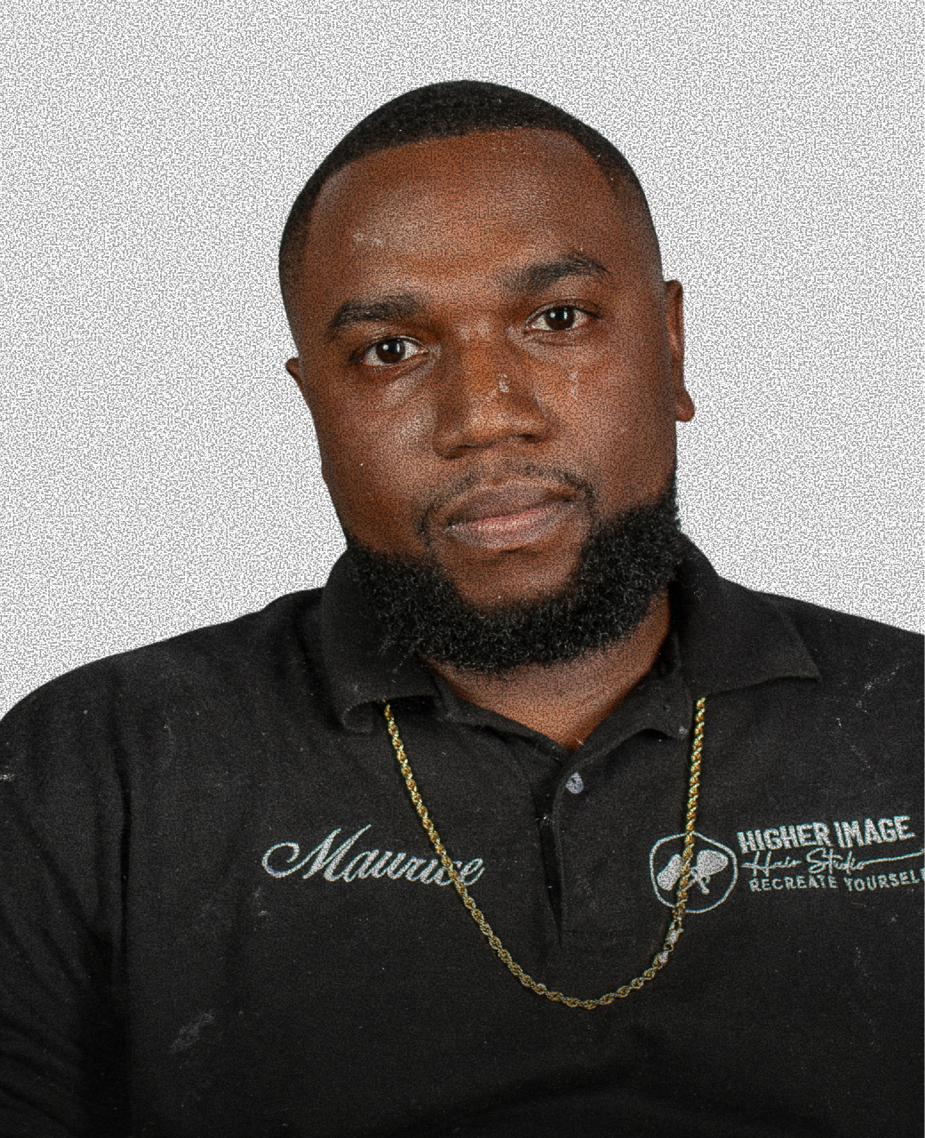 Portrait of a young man with a beard, wearing a black polo shirt with embroidered text, a gold chain, and a neutral background.