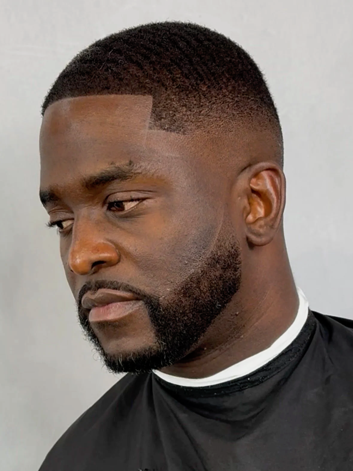 Close-up of a young man with a short haircut, beard, and dark shirt, looking to the side.