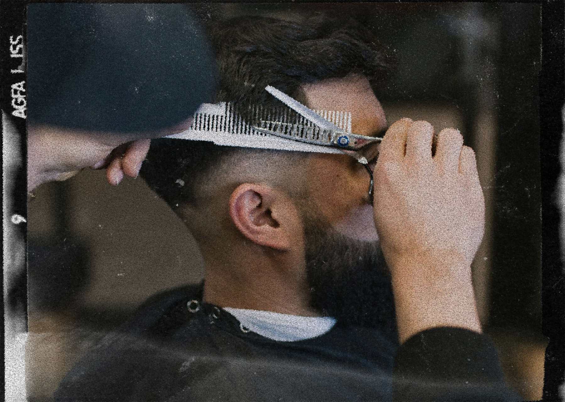 A barber using scissors to cut a man's hair, with the man�s head tilted forward and the barber�s hand holding a section of hair.