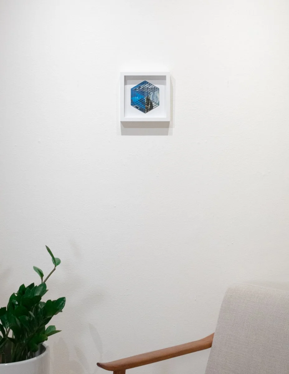 Image of embroidered collage in a white frame displayed on a wall above furniture