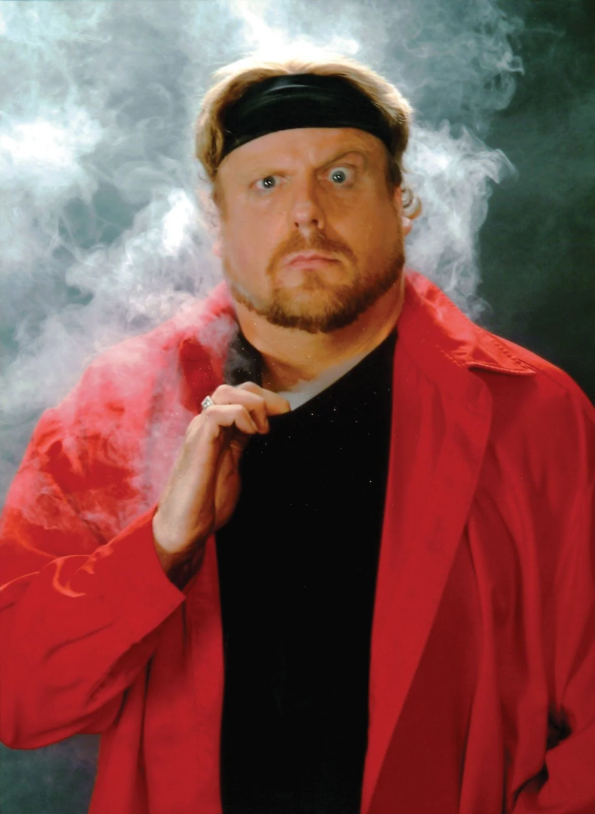 San Francisco magician the Amazing Johnathan in a red collared overshirt surrounded by smoke.