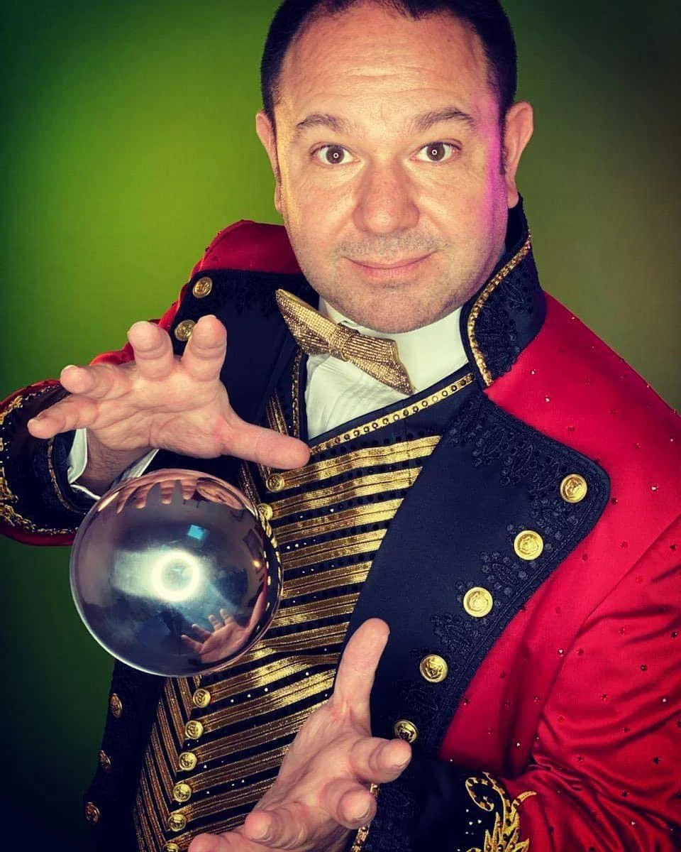 Robert Strong at virtual magic show in red showman's suit, performing floating orb trick