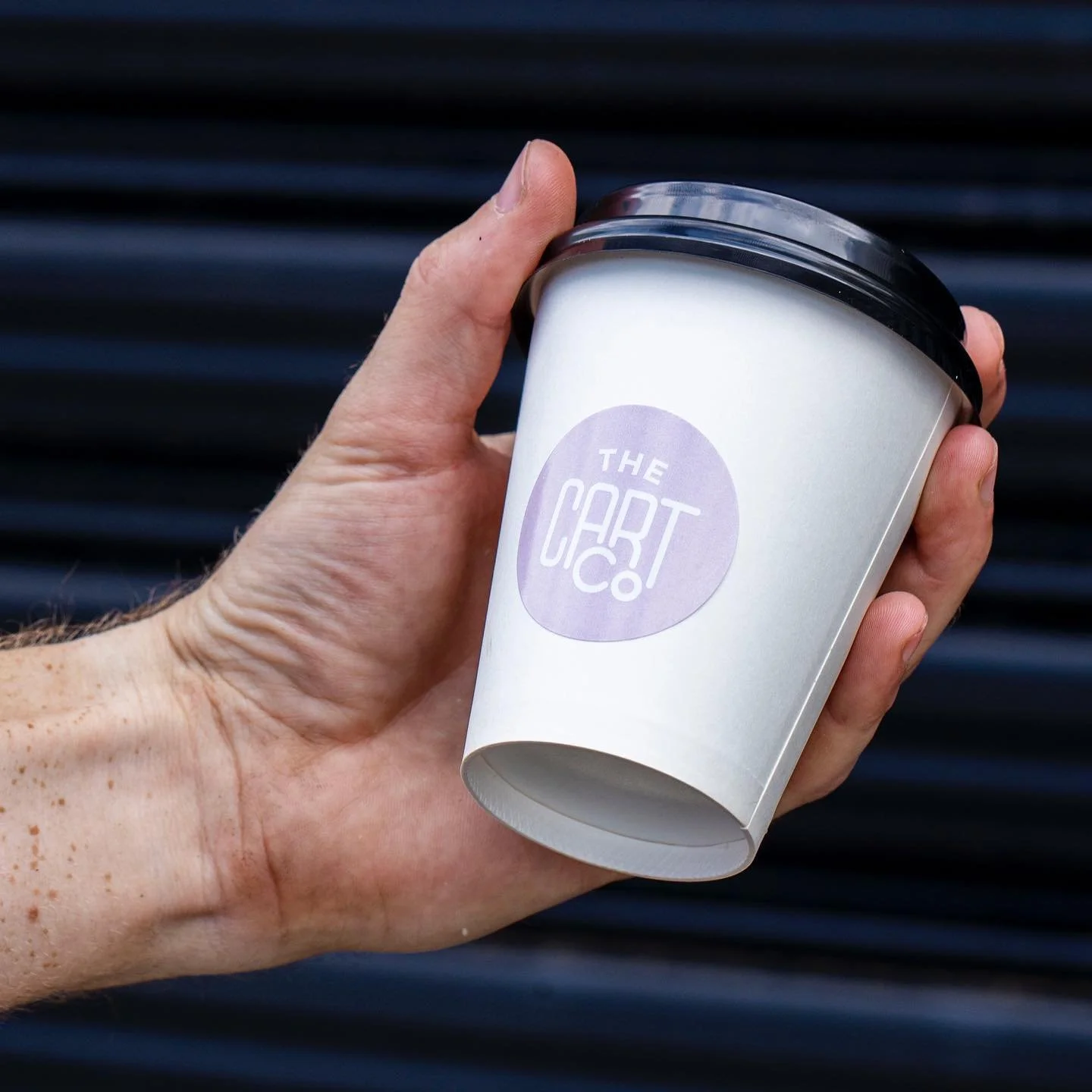 Hand holding a white The Cart Co branded takeaway coffee cup