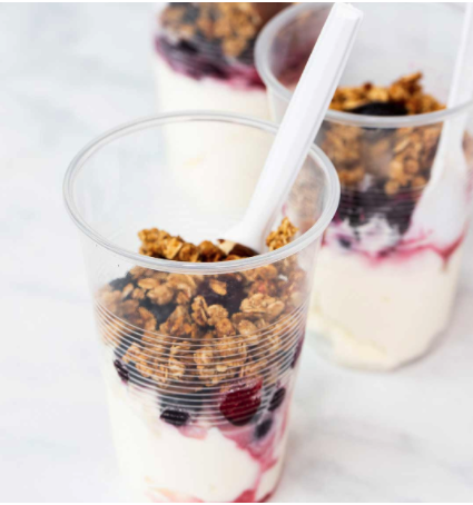 Clear cups of yoghurt with berries and crunchy muesli, served with spoons
