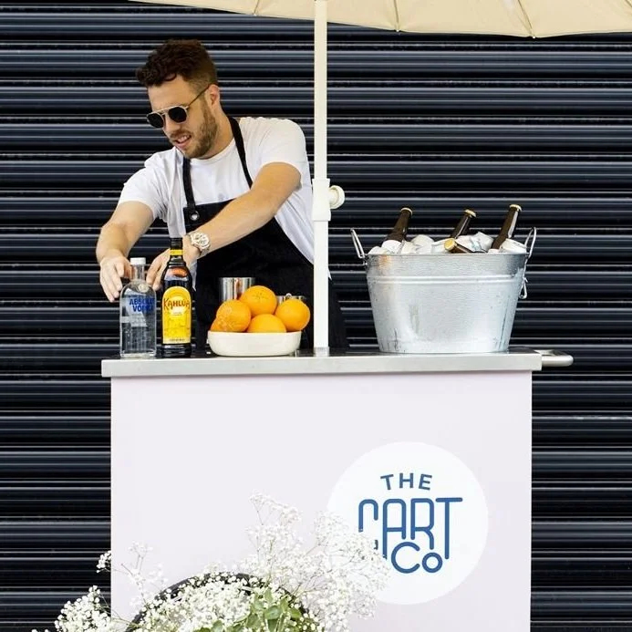 Bartender preparing drinks at a mobile bar with bottled spirits and fresh oranges