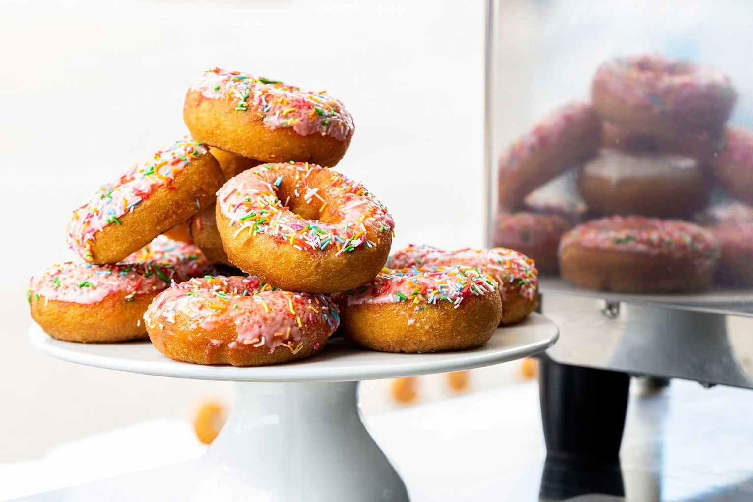 Pink iced donuts with colourful sprinkles on a white serving stand