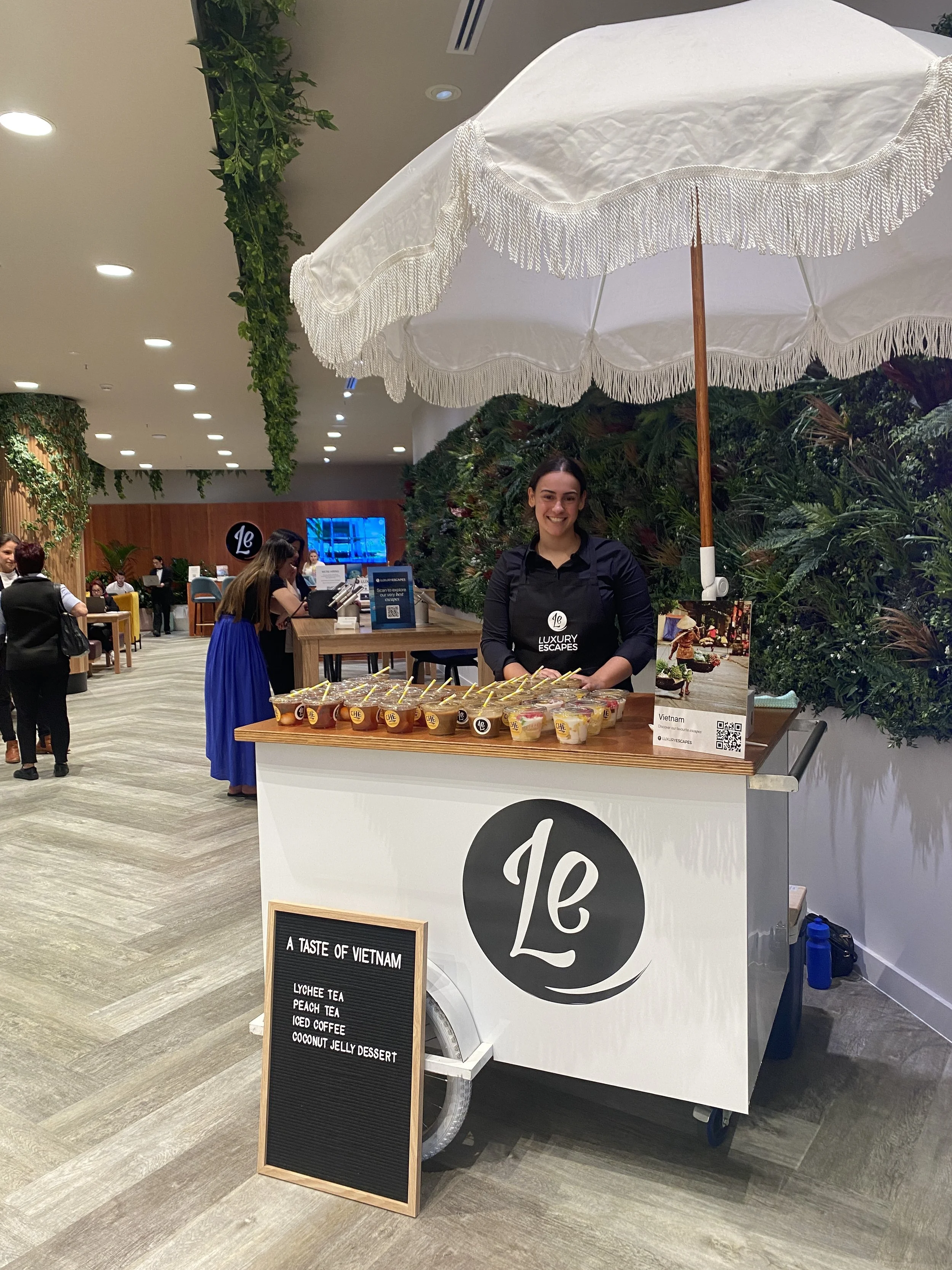 Luxury Escapes-branded event cart with white umbrella and a staff member standing behind it