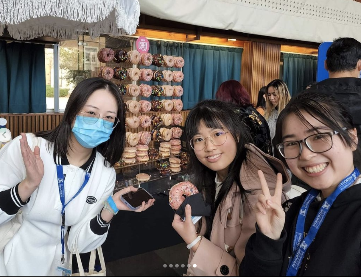 Three guests posing with donuts in front of a decorated donut wall