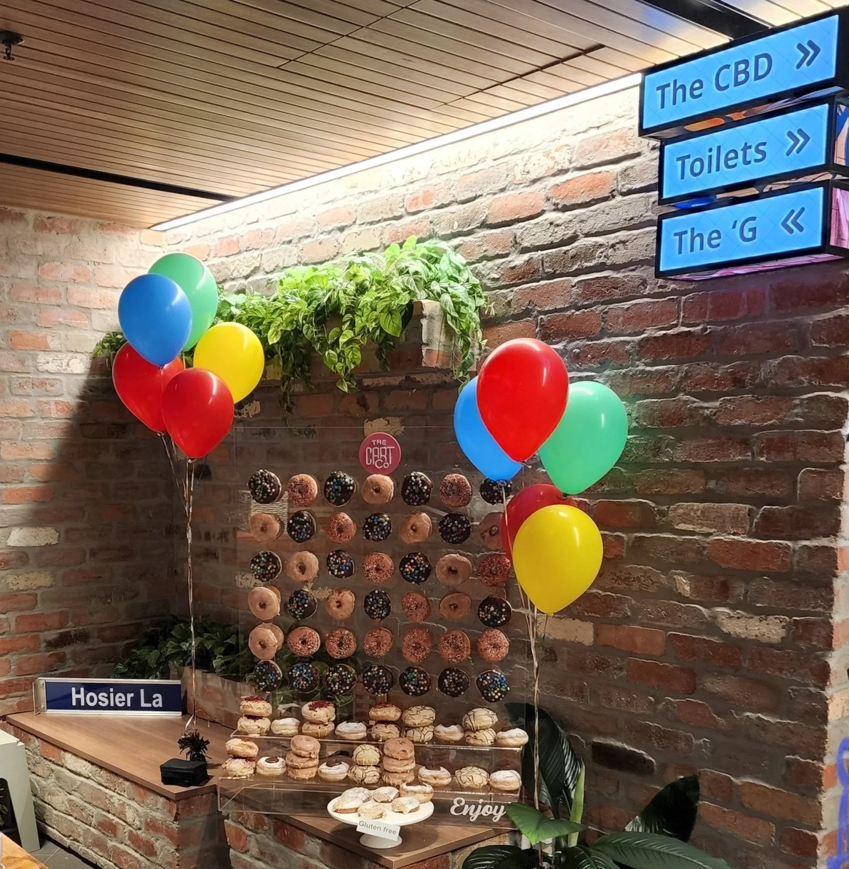 Donut wall with assorted decorated donuts and colourful balloons