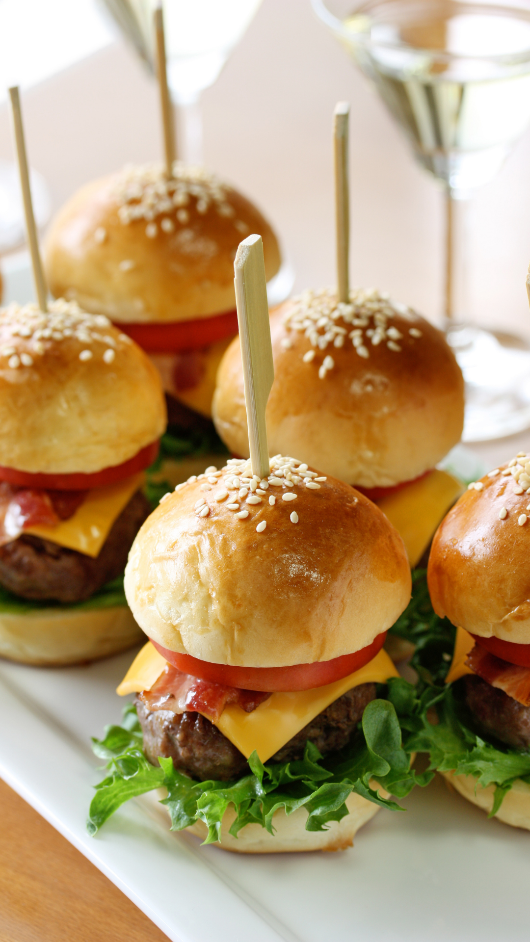 Mini cheeseburger sliders with lettuce and tomato on a white platter