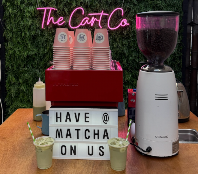 Matcha drinks and pink takeaway cups beside a sign reading Have Matcha on Us