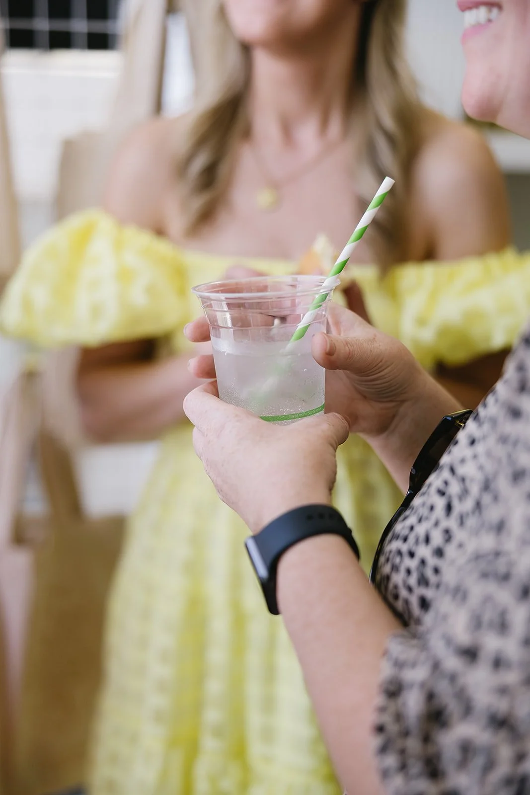 Guest holding a clear iced drink with a green-and-white striped straw