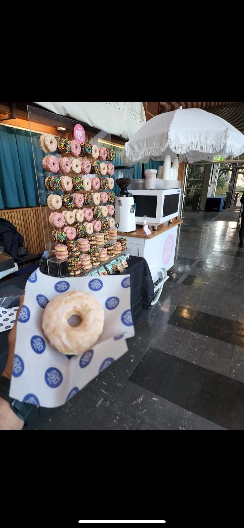 Donut wall with decorated donuts beside a white The Cart Co coffee cart