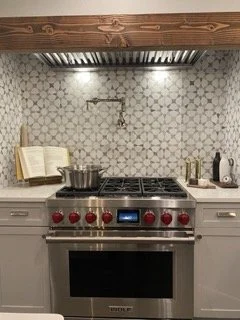 Kitchen stove with pots and utensils, open cookbook, and tiled backsplash.