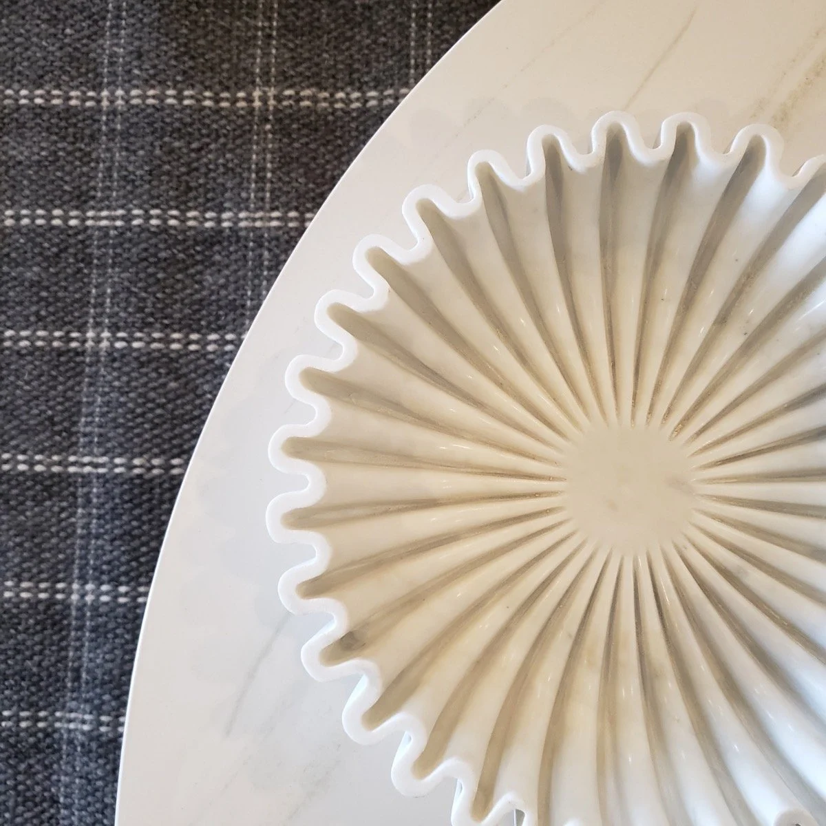White ceramic plate with a sunburst pattern, placed on a marble surface next to a dark, checked fabric.