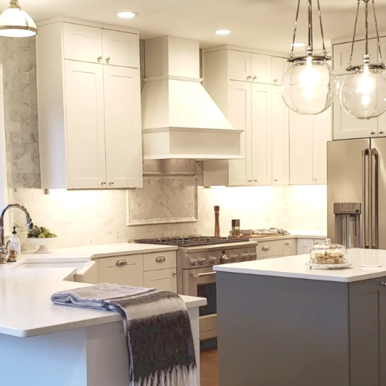 Modern kitchen with white cabinets, marble backsplash, stainless steel appliances, a kitchen island with a cake stand, and pendant lights.