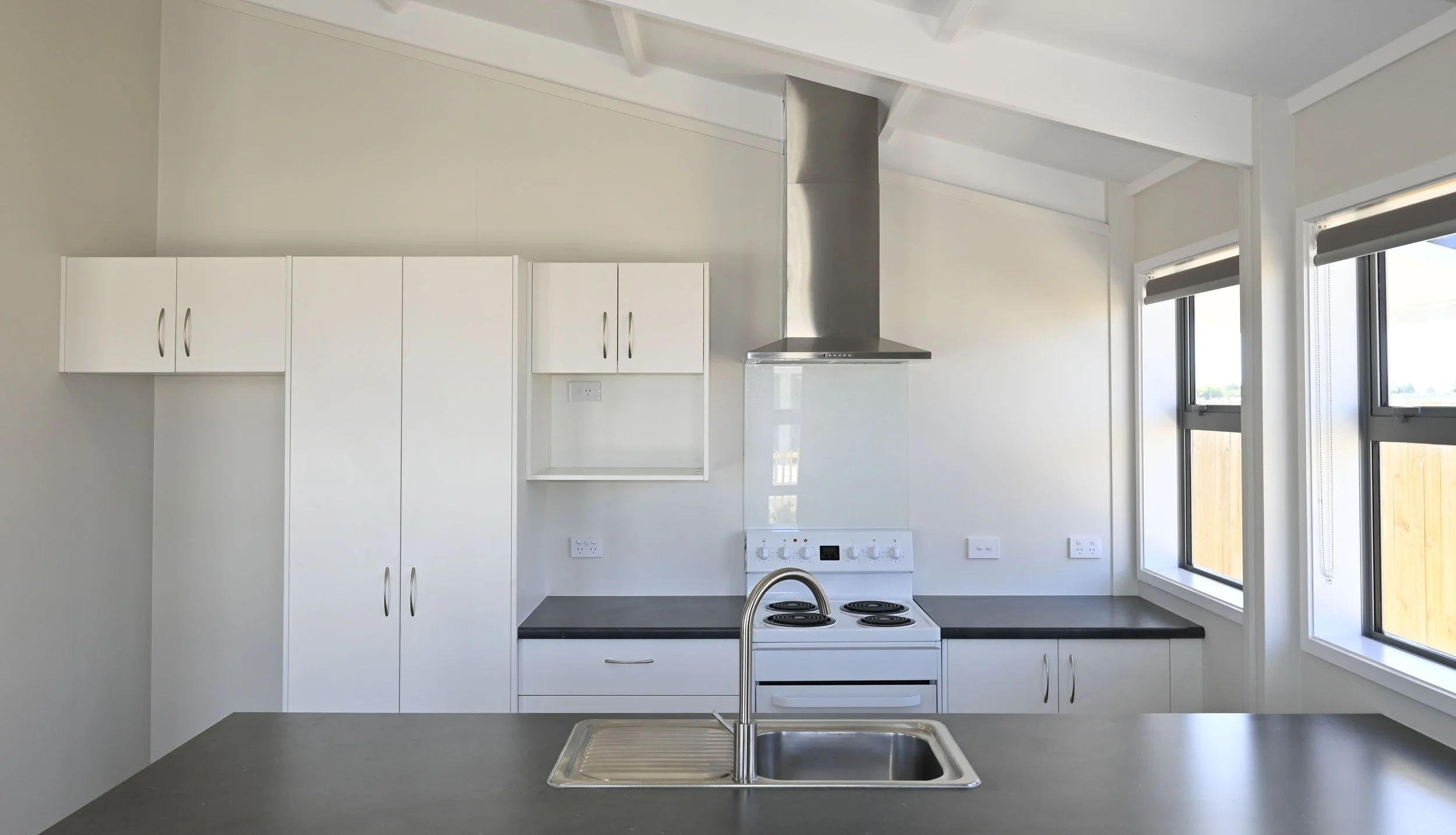 Large kitchen with oven, rangehood and dark bench-tops with large windows