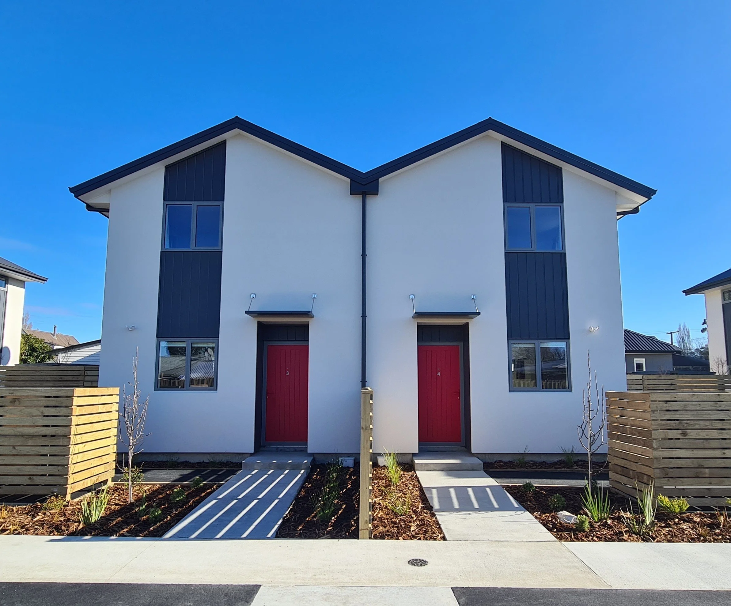 Exterior view of two-level homes with front-doors, paths and garden planting.