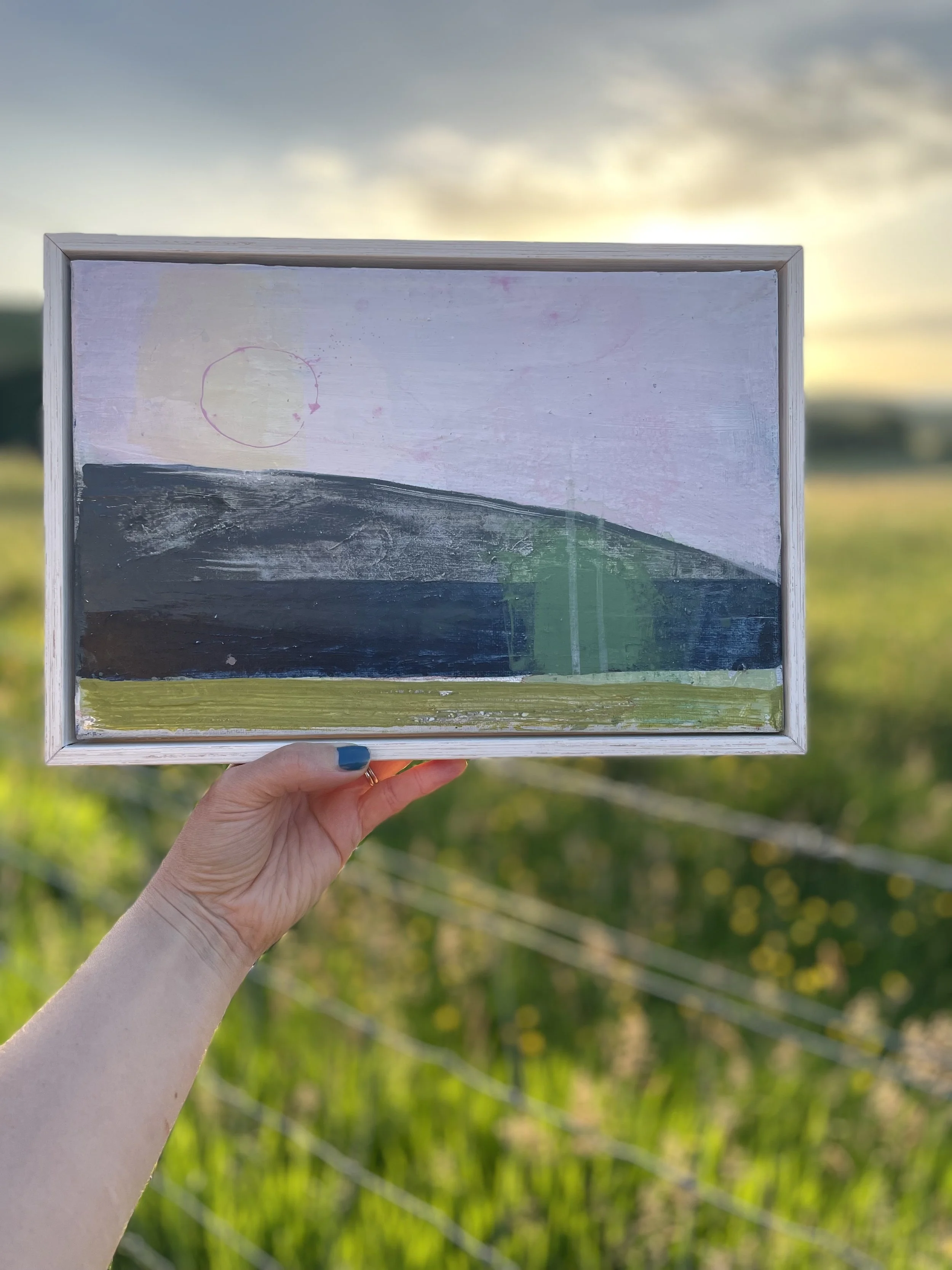 Gloaming 1 by Liz McQueen. A pale pink-ringed sun over a dark wooded hill, a single green tree and a bright line of the River Esk.