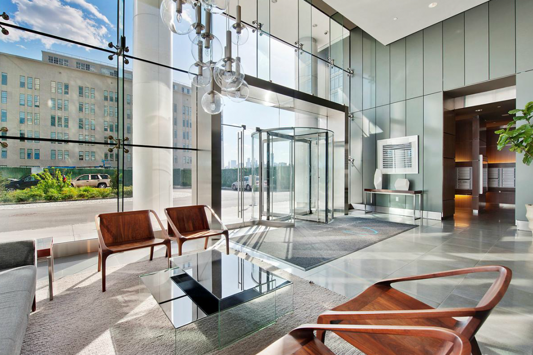 Modern hotel lobby with large glass windows, wooden chairs, a glass coffee table, and contemporary lighting fixtures.