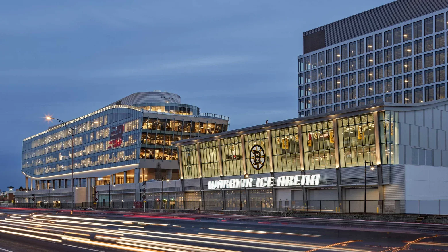 Exterior view of the Warriors Ice Arena in Boston with illuminated signs and modern glass architecture during dusk.