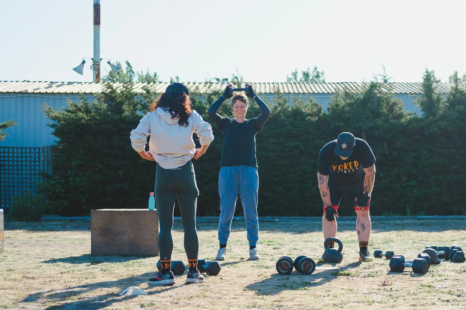 Yoked Fitness members exercise with kettle bells and dumbbells on the grass