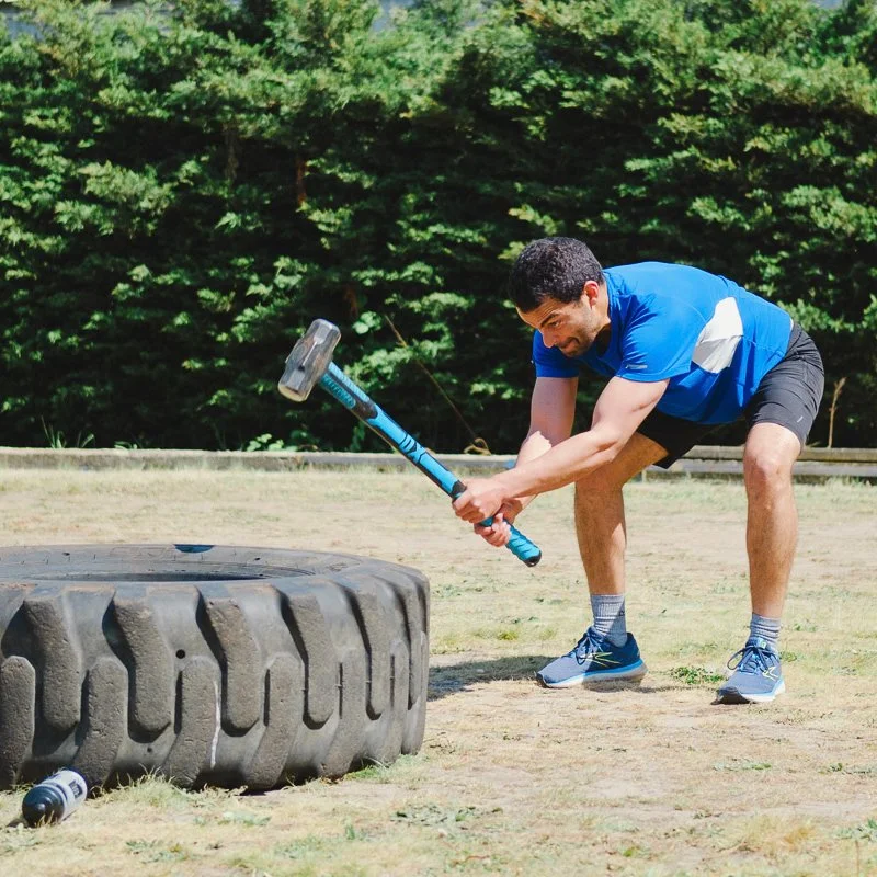 Male Yoked Fitness member hits a tyre with a hammer as a functional strength training exercise
