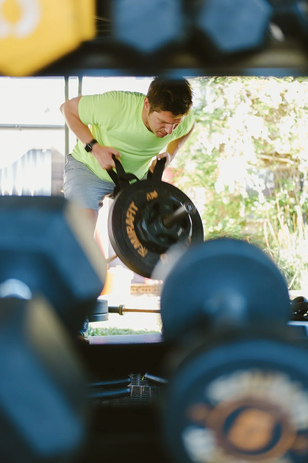 Yoked fitness member doing an inverted row framed by dumbbell weights in the foreground