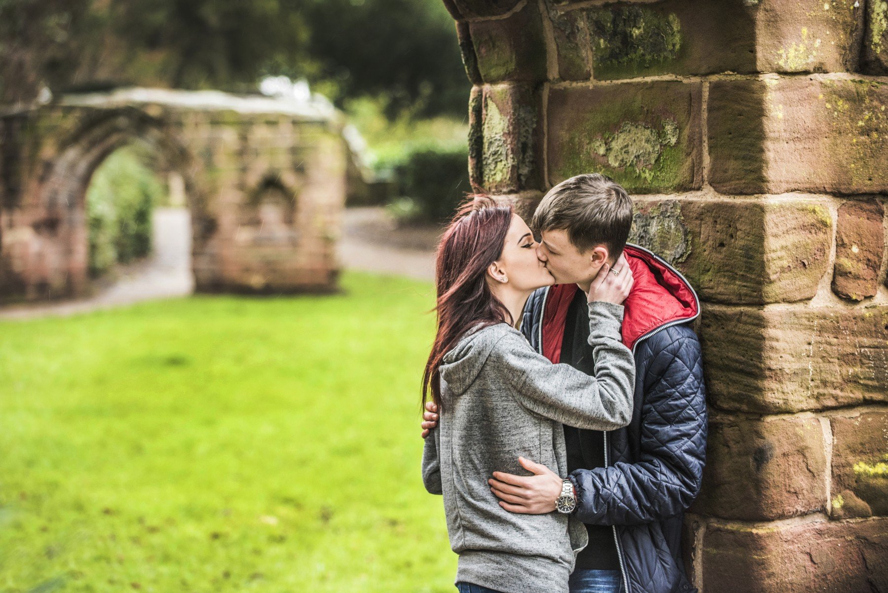 Man and woman kissing against red brick wall in Chester Roman Gardens