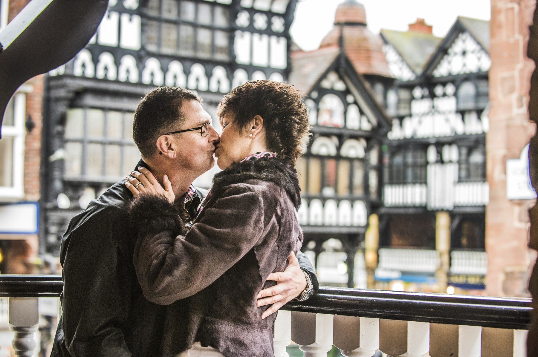 Man and woman kissing on Chester rows with tudor white and black buildings in backdrop