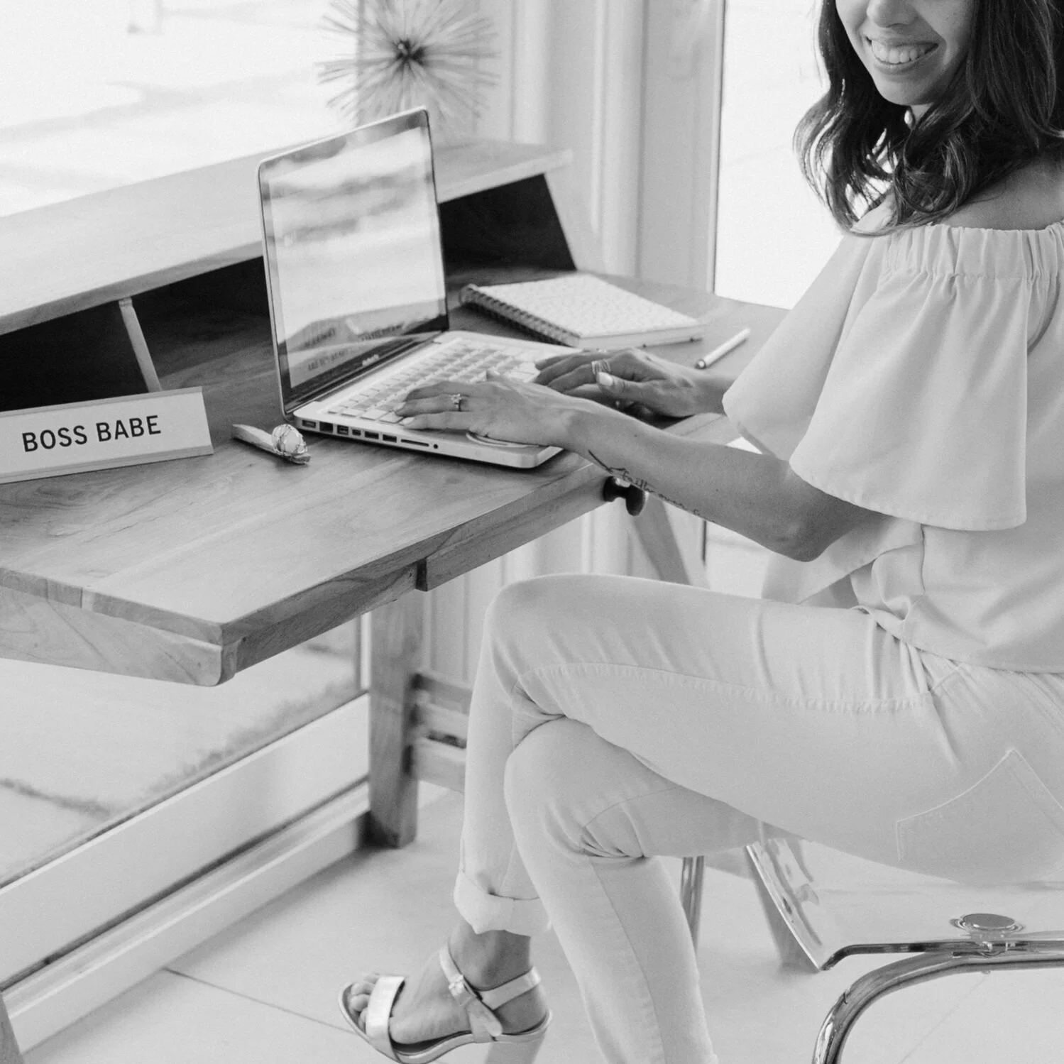 Woman sitting at desk using laptop, with a sign reading "BOSS BABE."