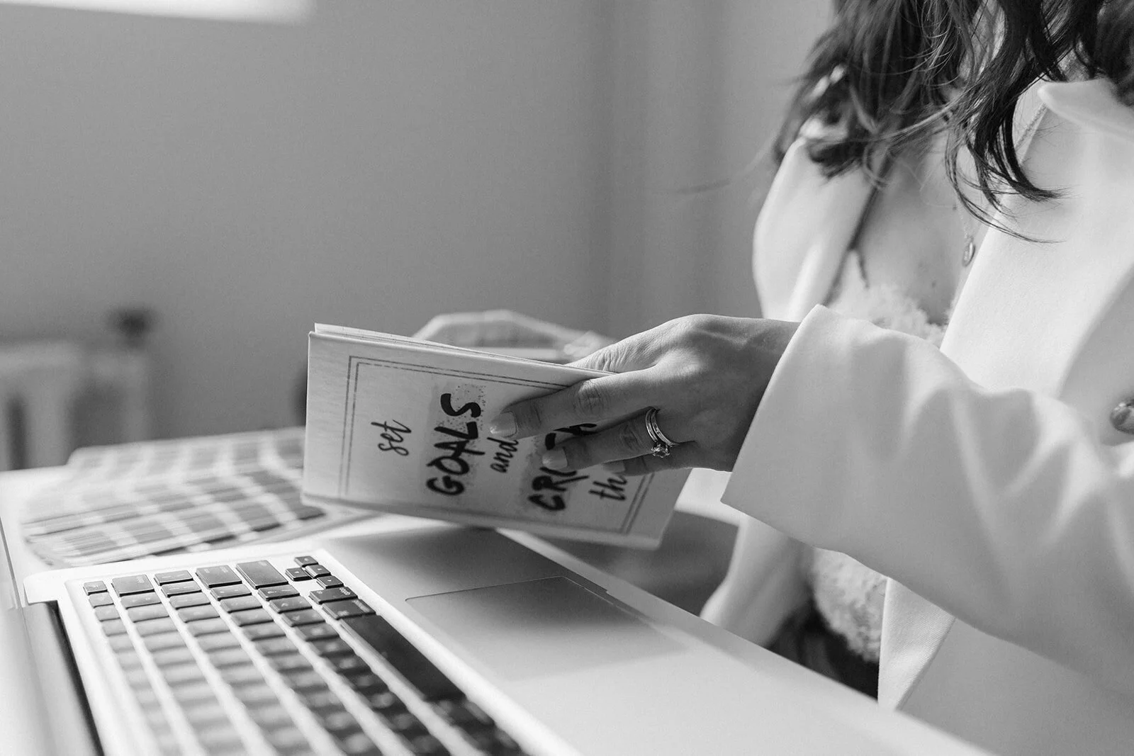 Black and white image of a person holding a card with text about setting goals, near a laptop keyboard.