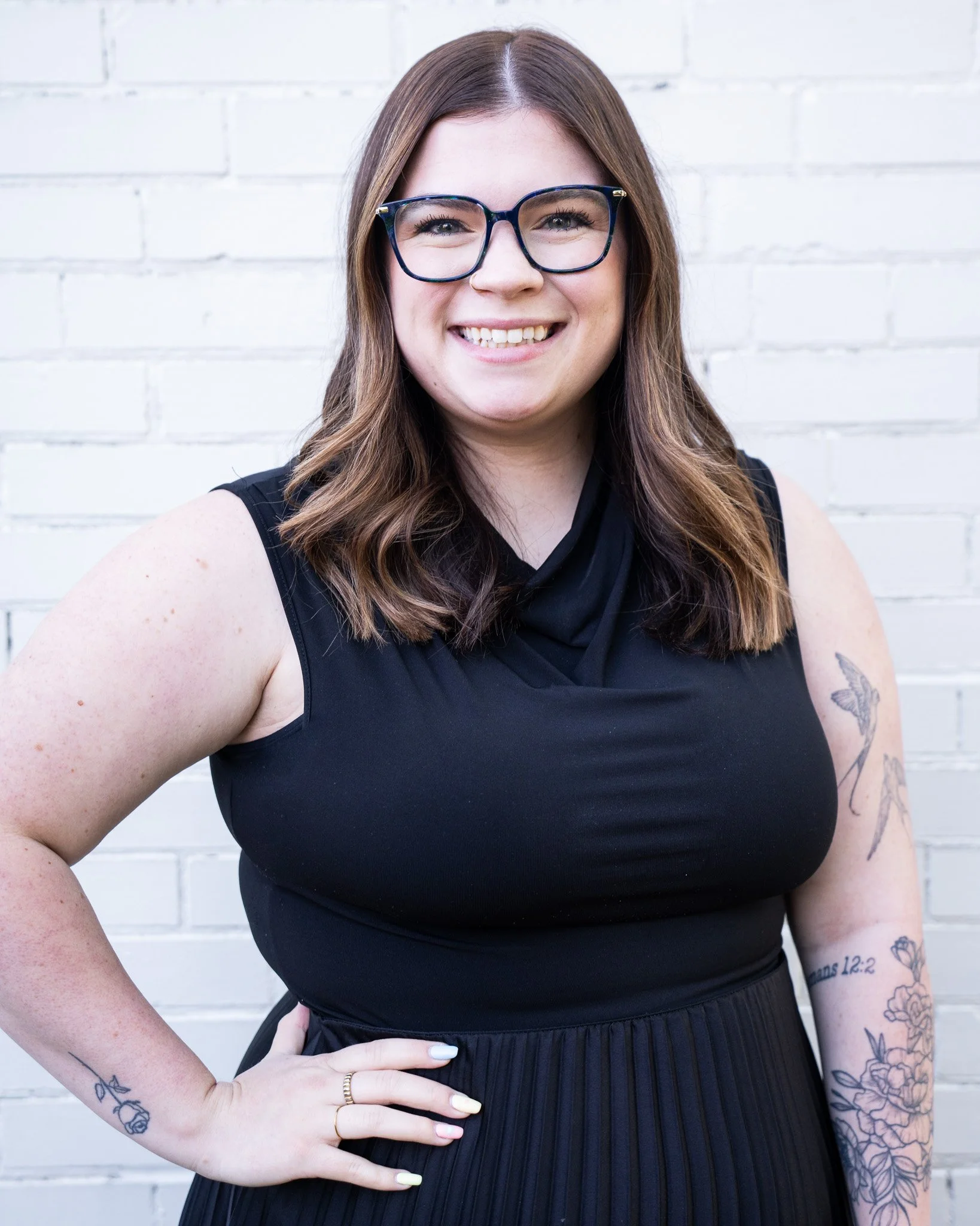 Headshot of Dorian Martinez, Coordinator, wearing a black dress and glasses with a white brick background
