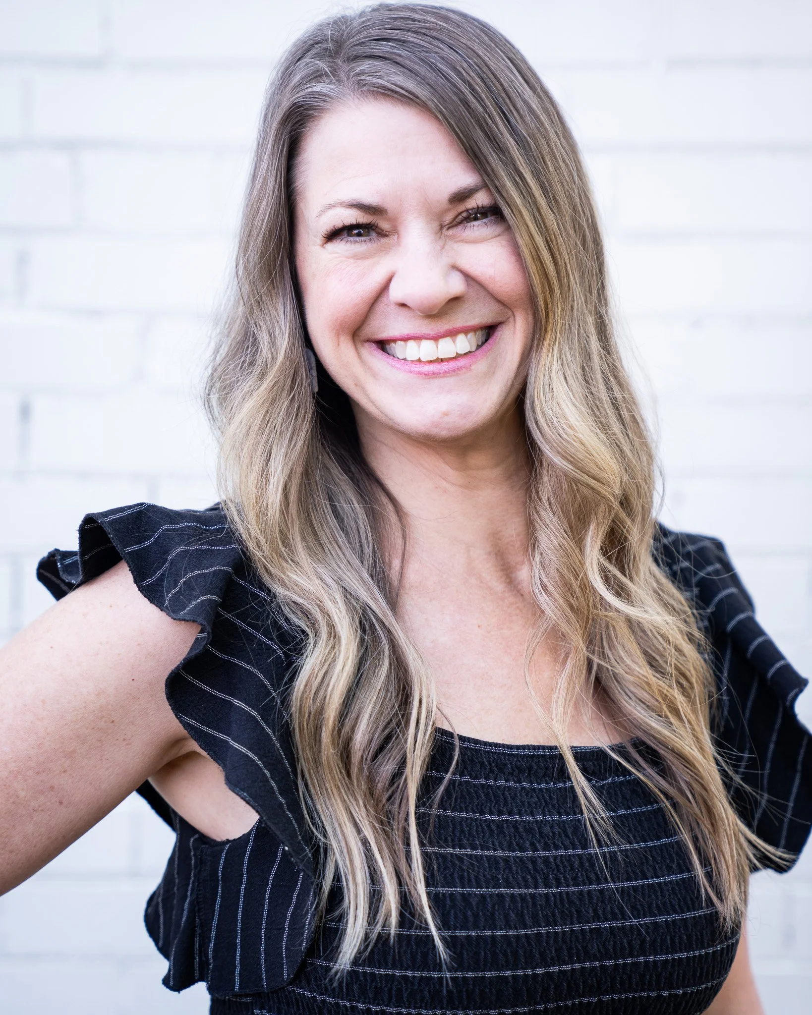 Headshot of Desiree, co-owner, smiling with a white brick background