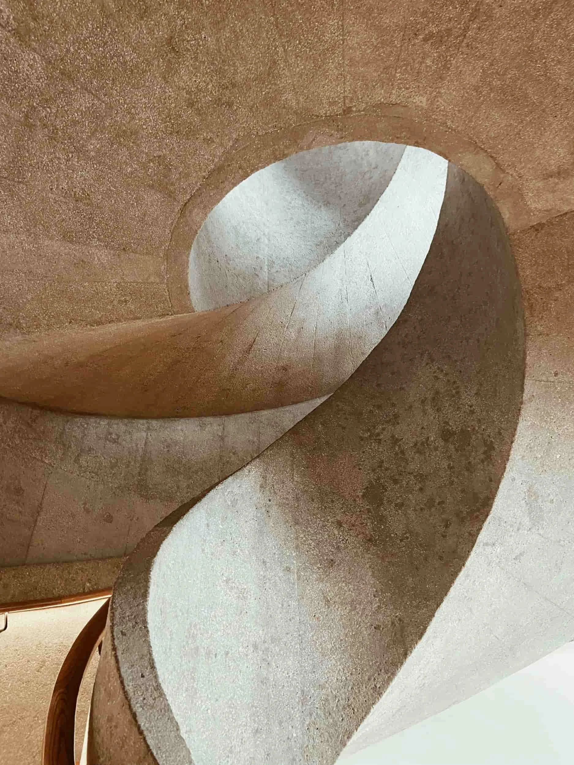 A spiral staircase with beige and gray walls, viewed from the bottom looking up.