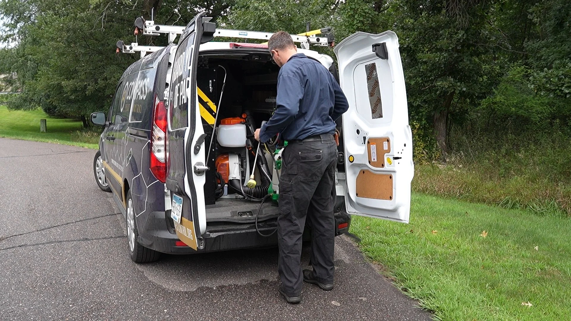 Compass Pest Control technician loading up backpack sprayer equipment for a residential exterior perimeter treatment.