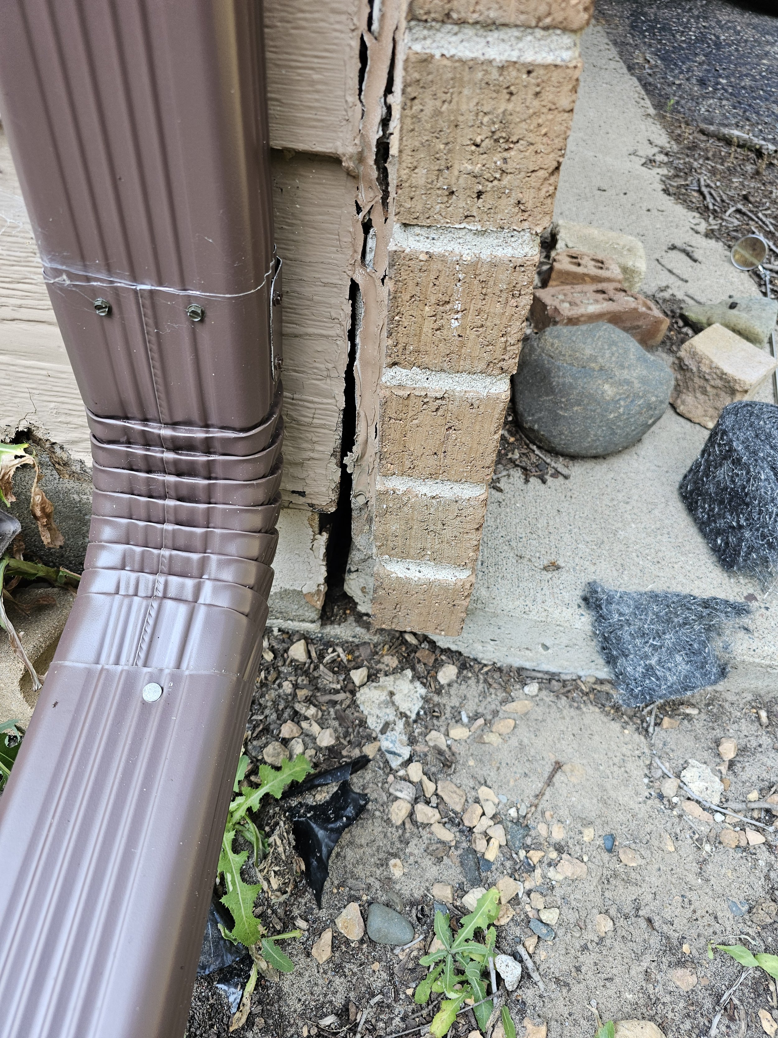 Gap between brick foundation and siding beside a downspout — a common rodent entry point that Compass Pest Control seals during exclusion work