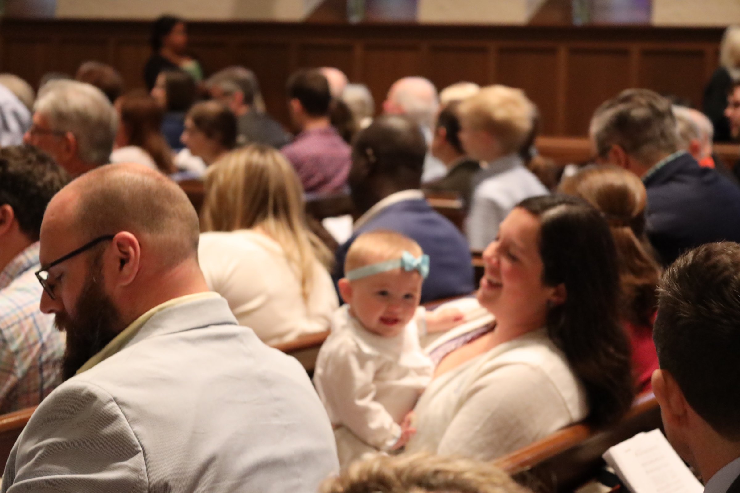 Audience seated in a wooden pews inside a church or chapel, attending a service or event.