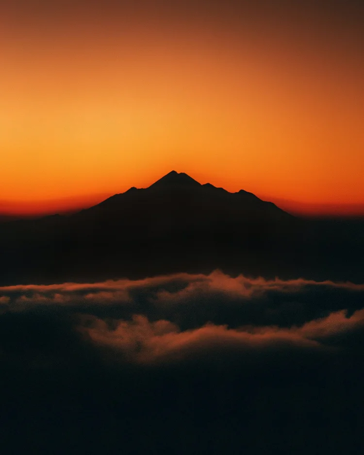 Mountain peak silhouetted against an orange sunset above a sea of clouds