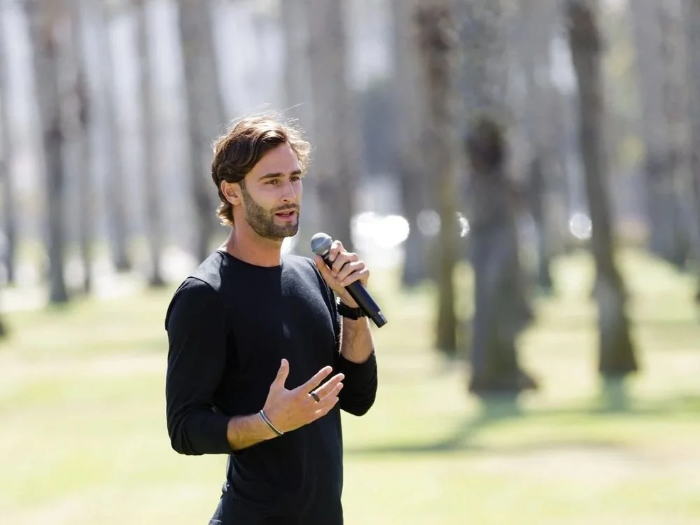 Sam Whiting teaching with a microphone in a grove of trees