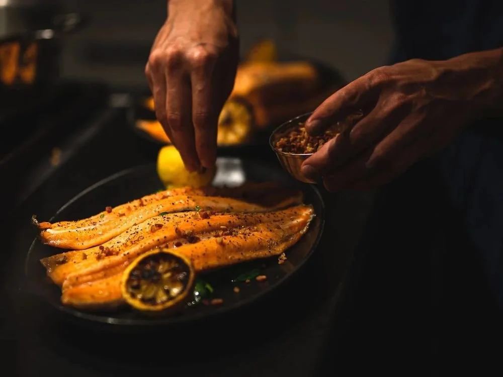 Hands squeezing lemon over a pan of seared fish