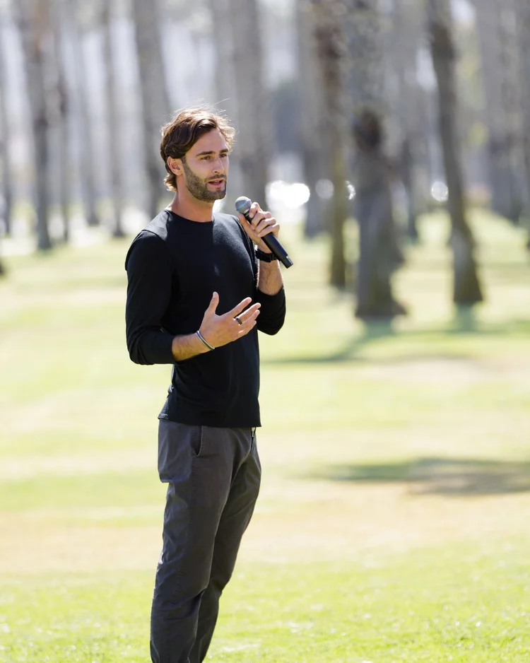Samuel Whiting speaking with a microphone outdoors under palm trees
