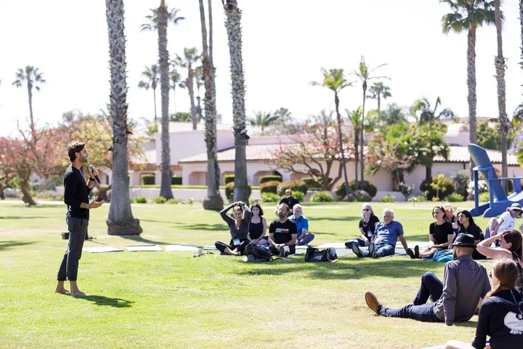 Group breathwork class on a lawn under palm trees