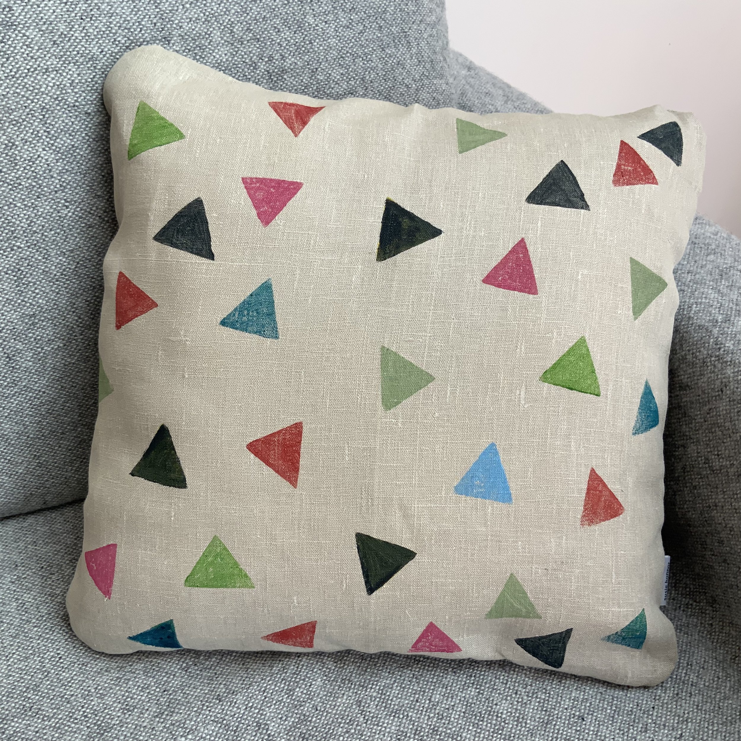 Potato printed cushion by Susie Honnor in Devon on 100% natural linen. Triangles in multicolours tumbling in space. Cushion is on sofa.