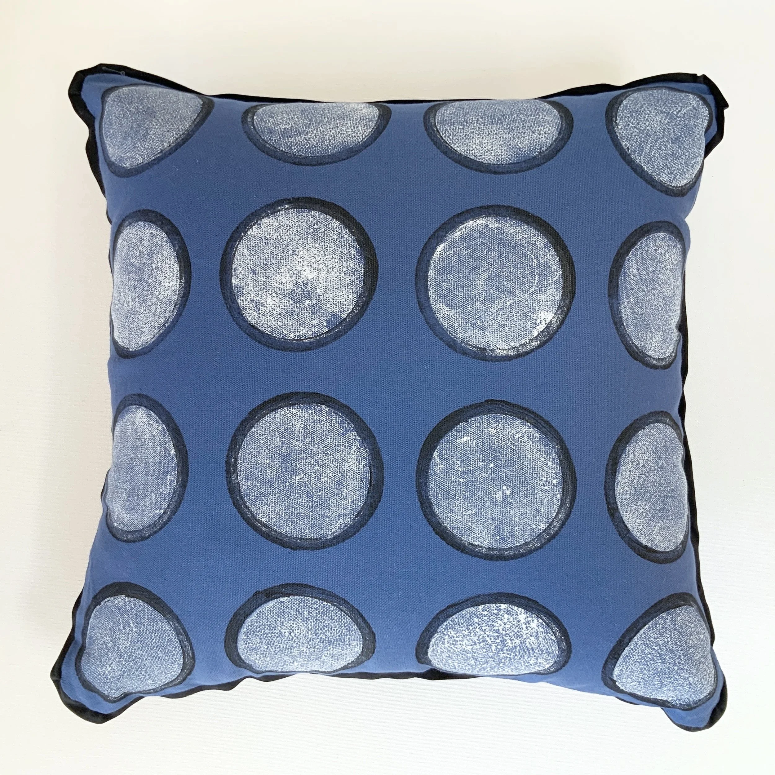 Hand printed cushion. Large white circles outlined in black are placed in grid formation onto a bright blue background fabric.