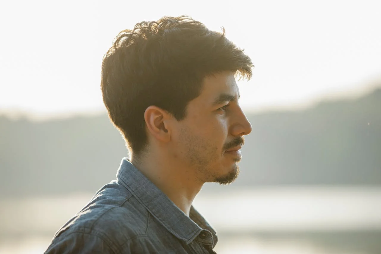 unemotional-bearded-man-standing-on-blurred-lake-background
