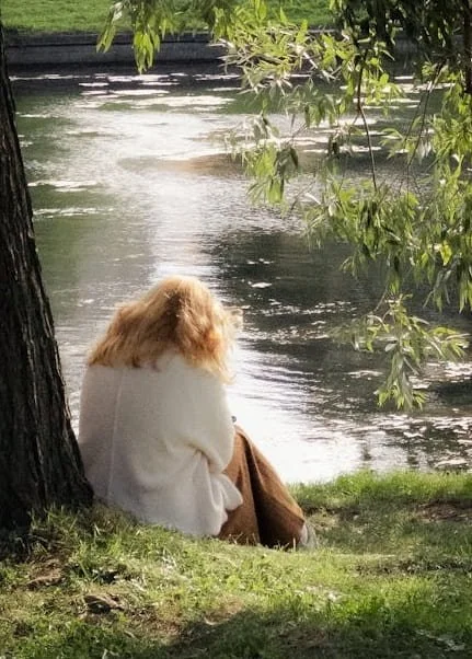 A woman alone under a tree by a river